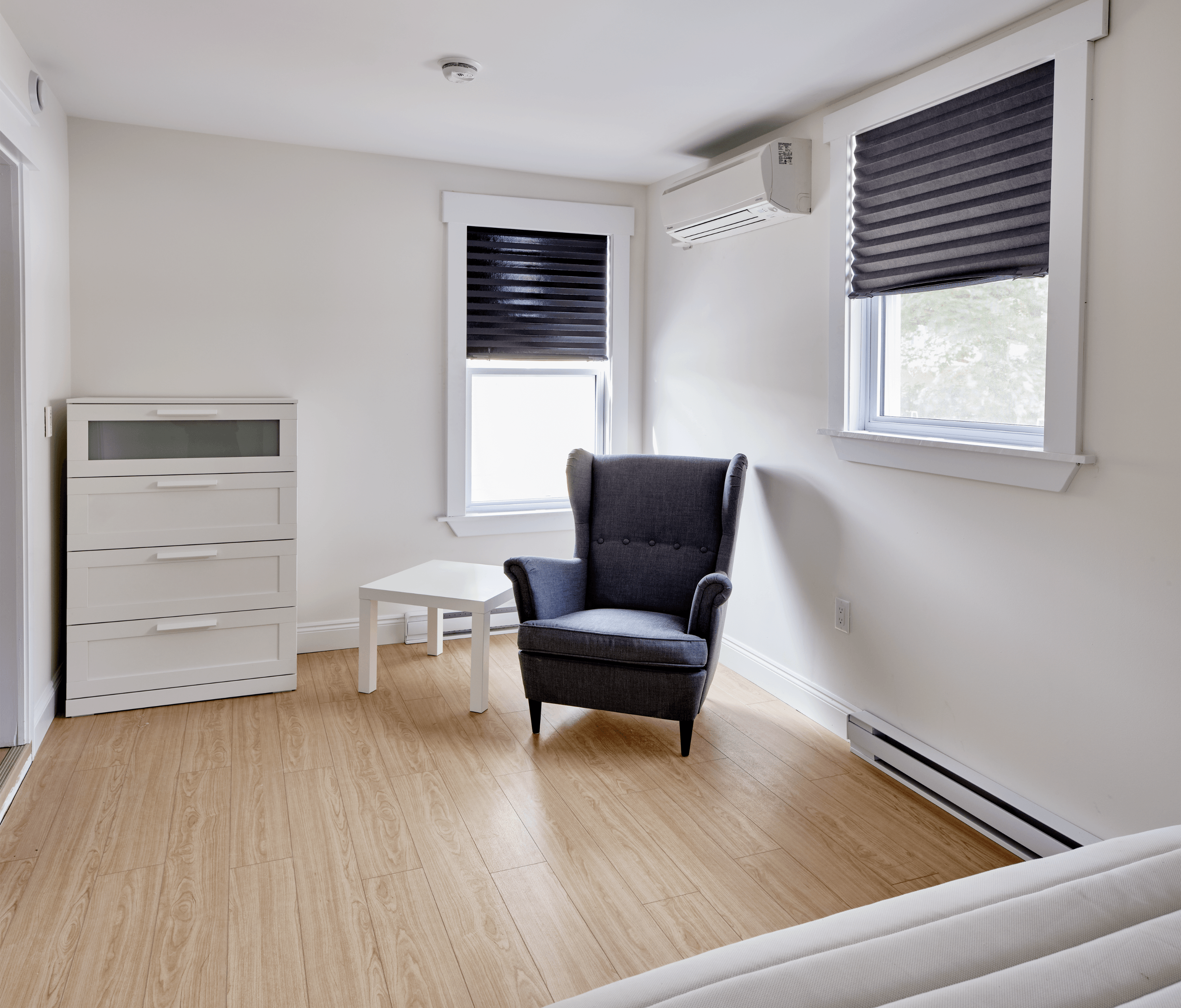 A black chair sits in a white room with a window and a white table.